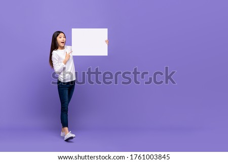Smiling cheerful Asian woman pointing hand to blank paper isolated on purple background with copy space