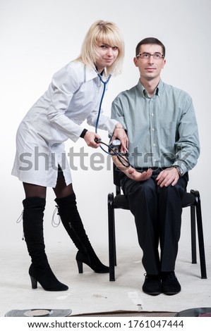 Female doctor in a white coat measures pressure to a man sitting on a chair, on a white background, isolated