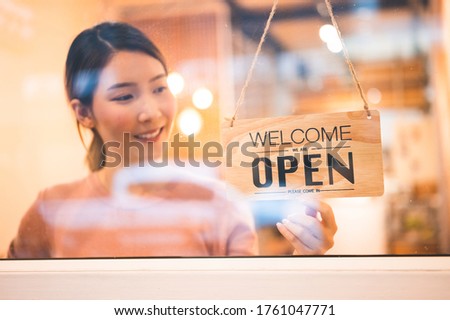 Asian woman store owner turning hanging open sign in front door of her shop