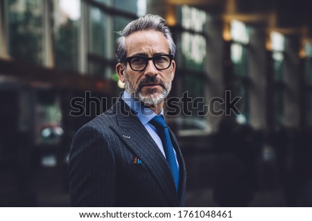 Portrait of serious middle aged businessman in elegant suit and glasses walking in downtown area of New York and looking away Royalty-Free Stock Photo #1761048461