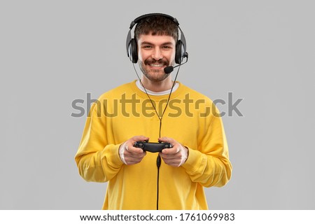 technology, gaming and people concept - happy smiling young man or gamer in headphones with gamepad playing and streaming video game over grey background