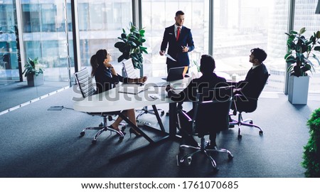Caucasian corporate boss explaining information during training conference meeting with male and female employees, experienced businessman dressed in formal suit holding paper financial report Royalty-Free Stock Photo #1761070685