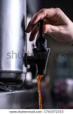 A Hand Opens the Faucet and Pours Rich Brown Tea From a Cafe Urn