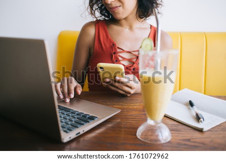 Cropped image of skilled woman using cellphone gadget and laptop computer for sharing media files during bistro visiting, female freelancer with mobile phone writing message during netbook chatting