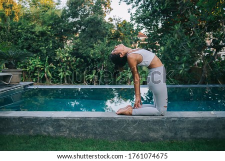 Calm flexible female in active wear reaching relaxation and inspiration during yoga practice near pool, good looking woman enjoying recreation during morning stretching training at patio porch