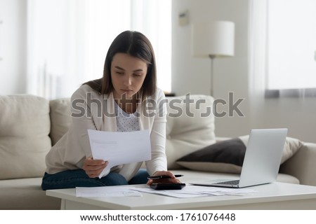 Serious woman sitting at coffee table full of papers documents, managing family budget. Businesswoman working with invoices, receipts, calculating expenses, taxes, bookkeeper do work from home concept Royalty-Free Stock Photo #1761076448
