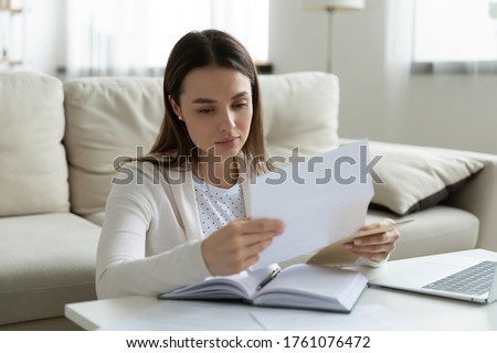 Woman sit at coffee table at home holding paper read personal touching letter from friend or relative looking like she missed or upset by sad news, frustrated female received postal message concept Royalty-Free Stock Photo #1761076472