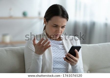 Irritated woman sit on couch holding smart phone feels annoyed network wi-fi connection lost, slow device, received unpleasant message bad sms, having problems with gadget, need repair service concept Royalty-Free Stock Photo #1761076520
