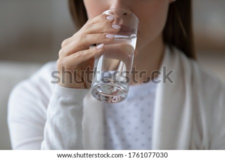 Close up image woman sit indoors holds glass of still or mineral water drinking clean aqua reducing thirst. Healthy lifestyle life habits, enough quantity every day for beauty skin health care concept Royalty-Free Stock Photo #1761077030