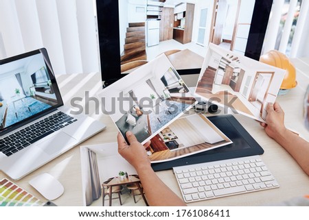 Interior designer sitting at desk and looking at printed photos of clients rooms after renovation
