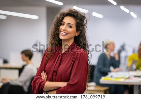 Successful businesswoman standing in creative office and looking at camera while smiling. Portrait of beautiful business woman standing in front of business team at modern agency with copy space. Royalty-Free Stock Photo #1761099719