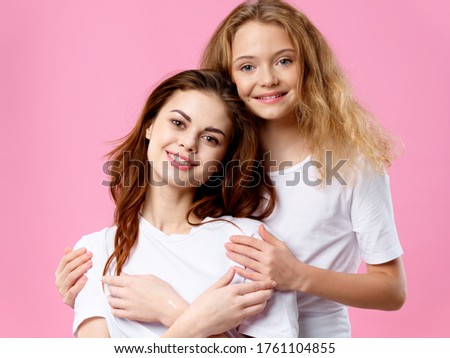 Beautiful girl hugs a happy woman on a pink background