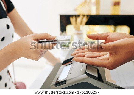 Close-up image of female customer giving credit card to bakery shop owner to pay for the order