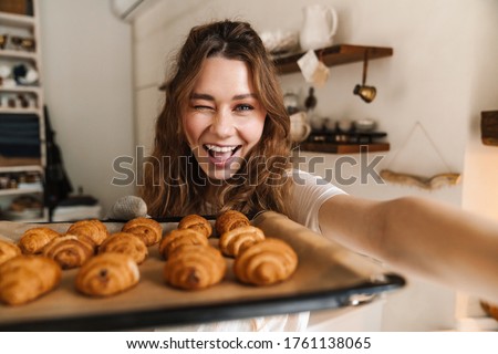 Cheerful young girl taking a selfie and showing baked cookies from the oven, winking