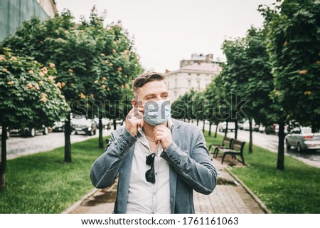Man puts on a face mask. Light blue face mask during a pandemic virus crown for protection against viruses and bacteria. Handsome businessman puts on a disposable mask on the street.