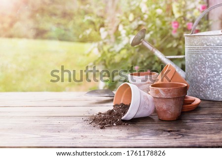 Terracotta pots & soil on a gardening bench outdoors on a sunny summer day. Extreme shallow depth of field with selective focus on center of table and blurred plants and garden shed in the background.