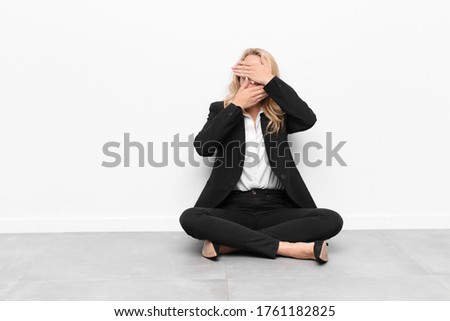 young blonde woman covering face with both hands saying no to the camera! refusing pictures or forbidding photos sitting on the floor