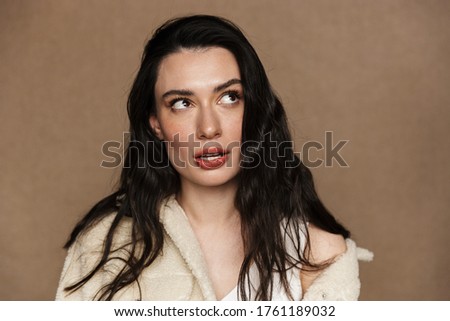 Photo of thinking young woman in jacket posing and looking aside isolated over beige background