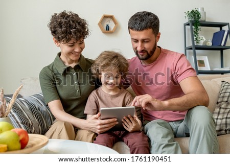 Cute little boy with touchpad and his young affectionate parents watching online video or movie or searching for curious cartoons in the net