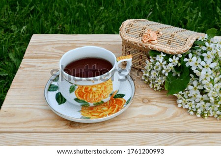 A cup of tea and a wicker box with blooming twigs on a wooden table with a napkin. Tea party, flowers, outdoors.