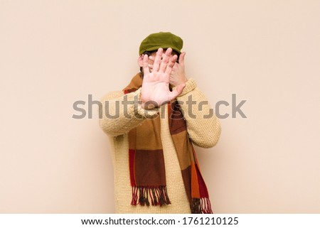 young cool bearded man covering face with hand and putting other hand up front to stop camera, refusing photos or pictures