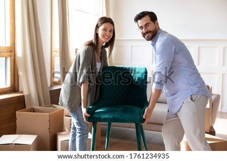 Portrait happy young couple carrying chair, placing furniture in living room in new house, looking at camera, moving day and renovation concept, excited family relocating into new apartment Royalty-Free Stock Photo #1761234935