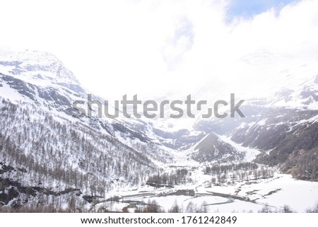 Picture of white cold moutain scenery, seeing from the train while passing an alpine with snowy weather and cloudy sky: Switzerland