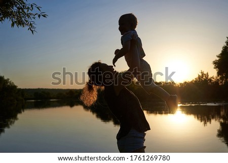 Mom throws up her son on the riverbank at sunset, the theme of summer fun.