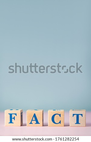 Wooden cubes with blue letters with word fact on pink and gray background with free space for text. False and real fact and concept of news. Statement of reality or what is happening.