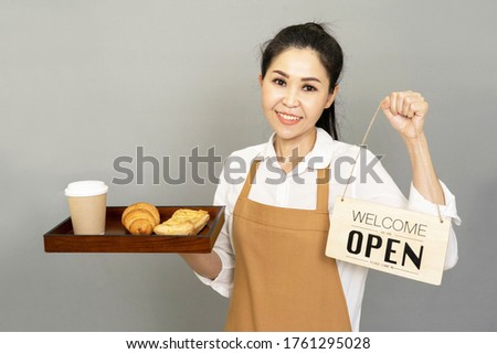 Small business owner happy young beautiful asian woman holding bread paper cups hot beverage and the sign for the reopening of the place after the quarantine, invite visit cafe 