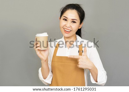 Small business owner happy young beautiful asian woman propose hand arm paper cups hot beverage invite visit cafe wear casual white t-shirt and rown apron isolated gray  background