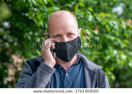 A Caucasian adult man in black protective mask is walking one along empty street and talking on phone. Safe behavior during quarantine and coronavirus pandemic. The new normal and modern reality