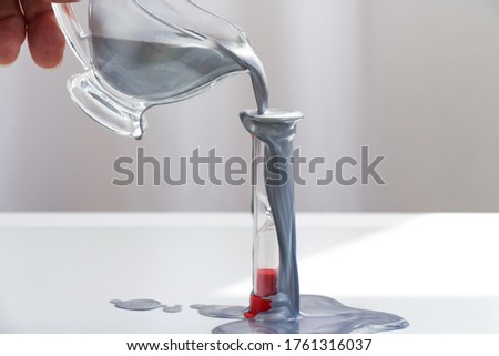 Silver paint pours on an hourglass. Hourglass on a white background. Silver pours from above. Close up.