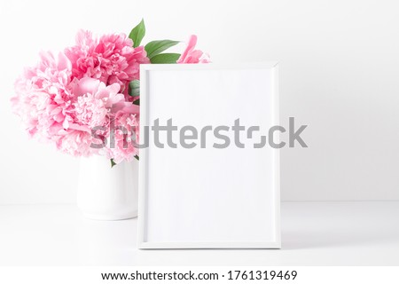 Home interior floral decor on white shelf. Front view blank mock up of photo frame. Beautiful flowers pink peonies in vase on white background.