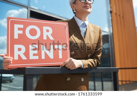 Close-up of real estate agent with placard For Rent standing outdoors