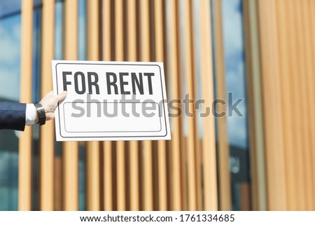 Close-up of man holding placard For Rent against the office building outdoors