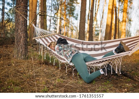 Young attractive woman laying in the hammock in sunny forest, resting after active hike - photo with selective focus
