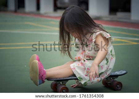 Toddler girl sitting on a penny board, skateboard at the basketball court.