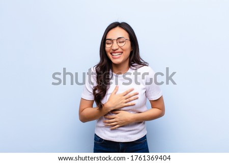 young latin pretty woman laughing out loud at some hilarious joke, feeling happy and cheerful, having fun against flat wall