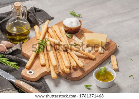 Traditional italian breadsticks grissini with rosemary, parmesan cheese, olive oil, garlic and salt on a gray background. Royalty-Free Stock Photo #1761371468