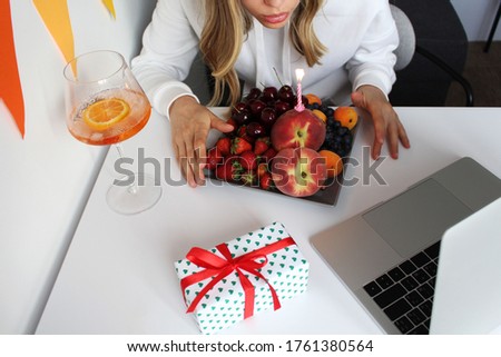Woman blowing out the candle on fruits and making video call. Concept of healthy lifestyle.