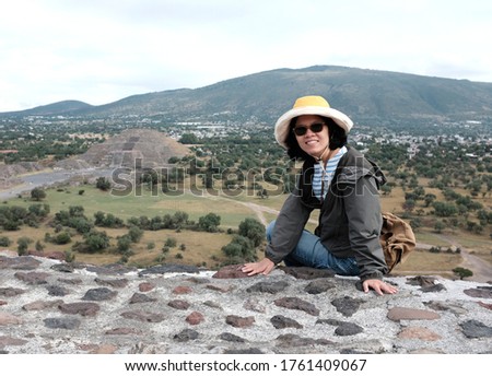 An Asian female tourist posing for a picture with a view of Pyramid of the Moon in Teotihuacán Municipality near Mexico City, Mexico in the background.