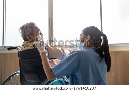 Asian nurse taking care of mature male patient sitting on wheelchair in hospital. Young woman and old man wearing surgical face mask for protection of covid 19 pandemic. Girl smile to elderly man. Royalty-Free Stock Photo #1761410237