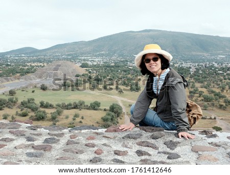 An Asian female tourist posing for a picture with a view of Pyramid of the Moon in Teotihuacán Municipality near Mexico City, Mexico in the background.
