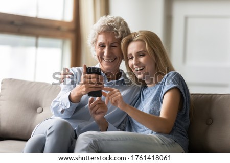 Elderly mom and grown up daughter watching funny video laughing having fun in internet, teenage granddaughter aged grandma having conversation by videocall, taking self-portrait on smart phone concept