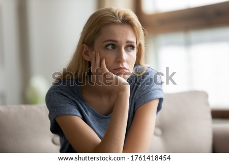 Concerned teenage girl sit on couch thinking lost in sad thoughts about split with boyfriend, romantic relationships break up. Woman having melancholic mood, divorce quarrel with beloved man concept Royalty-Free Stock Photo #1761418454