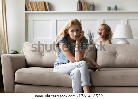 Screaming noisy little daughter brings mom to despair, parent feels tired resting seated on couch in living room. Hyperactive and naughty disobedient child, omission in upbringing or nurture concept Royalty-Free Stock Photo #1761418532