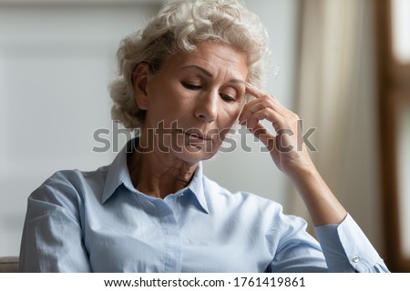 Close up head shot portrait sad depressed elderly 55s hoary woman looks concerned sitting on couch thinking about life troubles, goes through health problems, mental disorder or loneliness concept Royalty-Free Stock Photo #1761419861