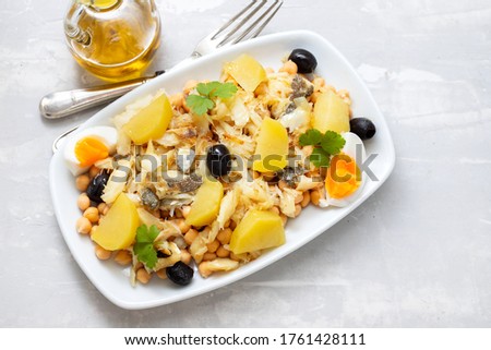 chick peas with cod fish, olives and boiled egg in white dish on ceramic background