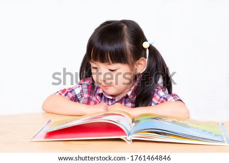 A little girl reading a book in front of a white background.